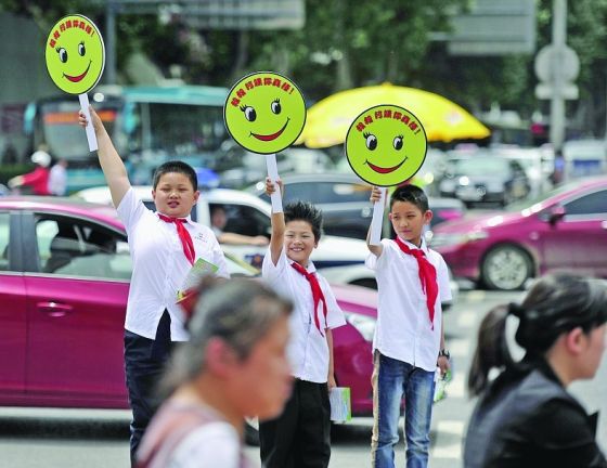 昨天，小学生交通志愿者在经七纬二路口向遵章过马路的行人举起“笑脸牌”。
