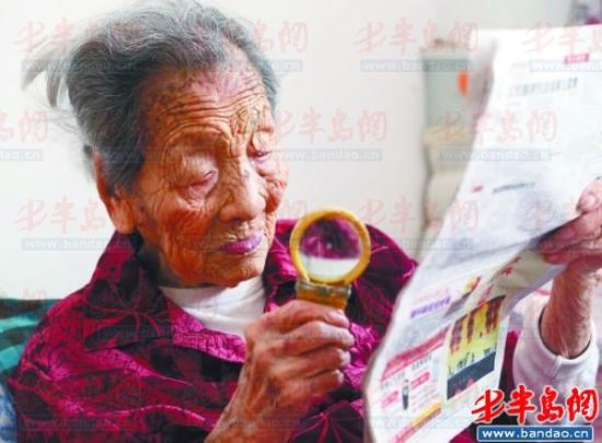 111岁的王玉玲老人拿着放大镜坚持每天看报纸，了解外边的事情。本报记者 王滨 摄