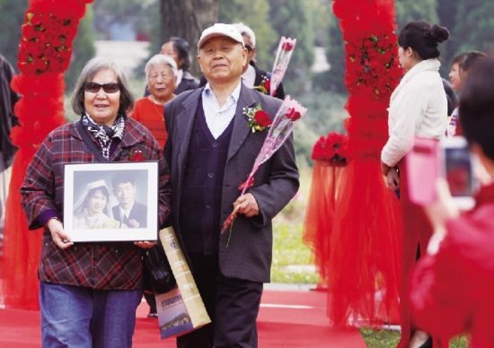 一对金婚夫妇携手走过玫瑰花门，手中捧着50年前的结婚照片。摄/法制晚报记者曹博远