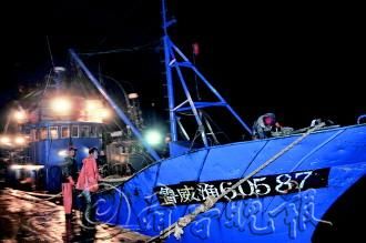 ▲14日晚,为躲避风浪,渔船靠港后,渔民在加固渔船。　记者　王震　摄