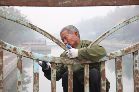  淄博市张店区玉龙河一座桥上,一名工人正在打磨栏杆,远处是灰蒙蒙一片,当日淄博空气质量等级为重度污染。